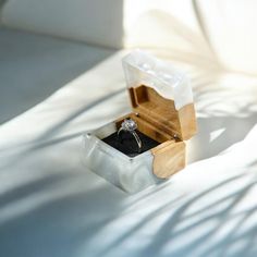 an engagement ring in a wooden box on a white surface with shadow from the sun