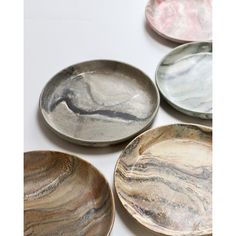 four plates with different designs on them sitting on a white table top, one is silver and the other is pink