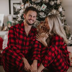 a man and woman in pajamas are sitting next to a christmas tree with a dog