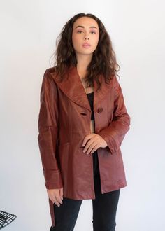 "Vintage 70s belted leather coat. The stand out on this bohemian classic is the oversized collar, buttons, and back pleated stitch detail. Wide wing collar. Long sleeves with wide cuffs. Front pockets. Front sash belt. Back waist panel with stitch detail. Large front button fastening. Fully lined. We kindly ask that you please view all measurements for comparison so you can get your desired fit. * Brand: Junior Gallery * Decade: 1970s * Fabric: 100% Leather * Lining: Satin * Color: Rustic Red C Vintage Leather Outerwear For Fall, Vintage Leather Outerwear For Spring, Vintage Long Leather Jacket For Fall, Vintage Leather Jacket With Lapel Collar For Winter, Retro Belted Fall Outerwear, Retro Belted Outerwear For Fall, Vintage Leather Outerwear With Lapel Collar, Vintage Leather Jacket With Lapel Collar For Fall, Vintage Longline Leather Jacket