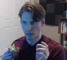 a young man is eating a doughnut in his living room while looking at the camera