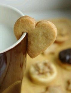 a heart shaped cookie is sticking out of a coffee cup with cookies in the background