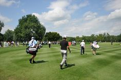 many people are walking around on the golf course, some carrying their bags and one is wearing a hat