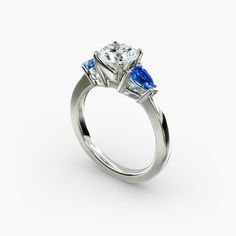 a three stone engagement ring with blue and white stones on the sides, set in 18k white gold