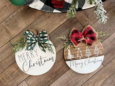 two wooden christmas ornaments with bows and merry lettering on them sitting on a wood floor