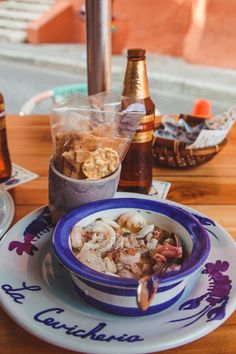 a bowl of food sitting on top of a wooden table next to bottles and glasses