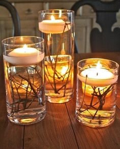 three glass vases filled with candles on top of a wooden table