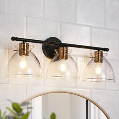 three light bathroom fixture with clear glass shades and brass accents on the wall above it