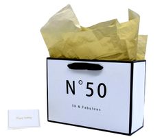 a white and black shopping bag with yellow tissue paper in it next to a card