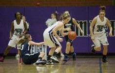 some girls playing basketball on a court with purple walls and people in the stands watching