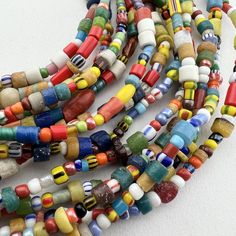 A long strand of vintage trade seed beads and Sand cast beads from Ghana in a lovely variety of Mixed African Trade Beads. Known as Christmas beads in the trade.  A really fun mixes of bright colors and interesting patterns and textures.  Our favorite way to wear them is on elastic wrapped around the wrist or waist or "as is" - a fun necklace. Approximate Bead Measurements: 24" of beads 28' with raffia 4-9mm diameter .8mm+ hole Hand-strung Heishi Beaded Necklaces, Traditional Spacer Beads For Festivals, Hand-strung Multicolor Round Beaded Necklaces, Handmade Heishi Oval Beads, Handmade Oval Heishi Beads, Traditional Heishi Beaded Necklaces, Multicolor Hand-strung Beaded Necklaces With Oval Beads, Traditional Colorful Beads For Crafting, Traditional Beaded Bracelets With Tiny Round Beads