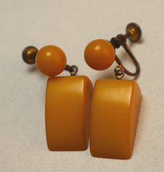 "Fun vintage butterscotch plastic earrings are an asymmetrical wedge dangling from a round bead in goldtone metal screw-down backing. The color looks like butterscotch bakelite but it doesn't sound or smell like bakelite. Still great chunky earrings, unmarked and 1 1/2\" long. Nice vintage condition with no issues." Vintage Orange Dangle Earrings, Vintage Orange Pierced Earrings, Vintage Amber Dangle Earrings, Vintage Orange Clip-on Earrings, Vintage Orange Earrings, Plastic Earrings, Chunky Earrings, Ball Earrings, Gold Tone Metal