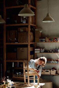 a woman working on a chair in a room with lots of shelves and hanging lights