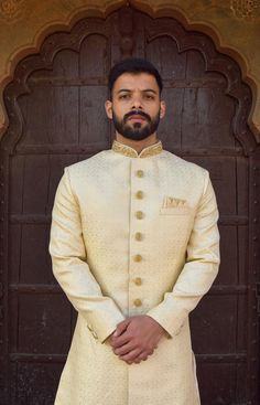 This white Sherwani has a distinctive mandarin collar and a row of buttons down the front. It features long sleeves and has a golden woven pattern on it. The matching churidar pants are also made with the same golden woven design. The included dupatta is made of golden net and has a similar design to complete the look. The Sherwani is made of imported fabric and is available in white colour. The package includes the Sherwani, Churidar pants (which are styled without any specific design) and a similar type of Dupatta. This elegant Sherwani suit is ideal for formal events, parties and evening dinners. Customization options are available for size, design and colour to suit your personal style and taste. We can also give you a turban, jooti, mojari of your matching outfit (additional cost will White Sherwani For Men, White Sherwani, Mens Wedding Suits, Sherwani For Men Wedding, Sherwani For Men, Delicate Clothes, Matching Outfit, Woven Pattern, Wedding Suits Men