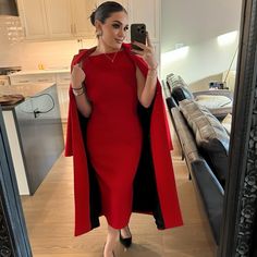 a woman taking a selfie in a mirror wearing a red dress and black cape