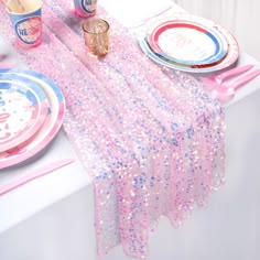 a table set with pink and blue plates, napkins, cups, and candles