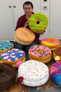 a man sitting on the floor with many different types of doughnuts