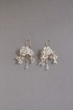 two white flowers are hanging from silver earwires on a gray background with pearls and crystal beads