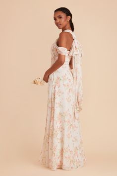 a woman in a white floral print dress with her back turned to the camera and holding a bouquet