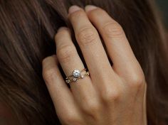 a woman's hand with a diamond ring on her left hand and the other hand holding it up to her ear