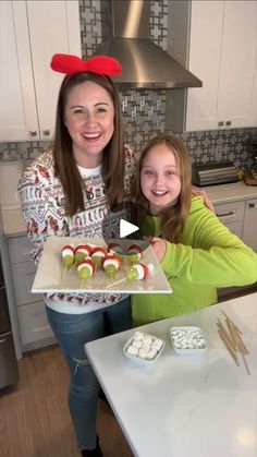 two girls in the kitchen with some food on a tray and one girl is smiling at the camera