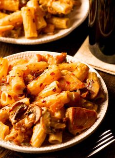 two plates filled with pasta and meat on top of a wooden table next to a glass of beer