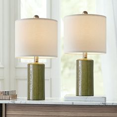 two green lamps sitting on top of a table next to a book and lamp shade