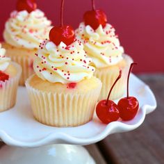 cupcakes with white frosting and cherries on a plate