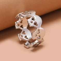 a silver ring with skulls and hearts on the inside, sitting on top of a beige surface