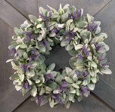 a wreath is hanging on the side of a wooden door with purple and white flowers