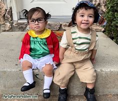 two young children sitting on the steps wearing clothes and hats, one with eyeglasses