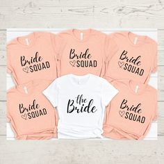 six bride squad shirts on top of a white wooden table with pink and peach colors