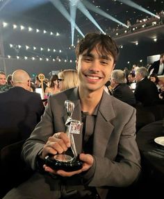 a man sitting in a chair holding an award at a awards ceremony with other people around him