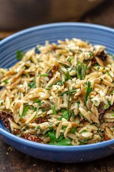 a blue bowl filled with pasta salad on top of a wooden table