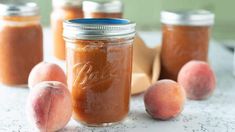 peach jam in a mason jar surrounded by peaches on a counter top, with the jars lined up and ready to be filled