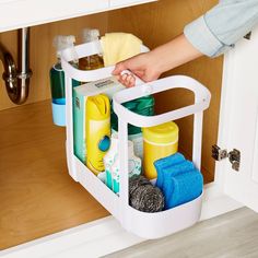 a person is holding a basket with cleaning products in it while standing next to the sink