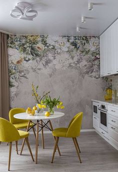 a dining room table with yellow chairs next to a wallpapered kitchen countertop