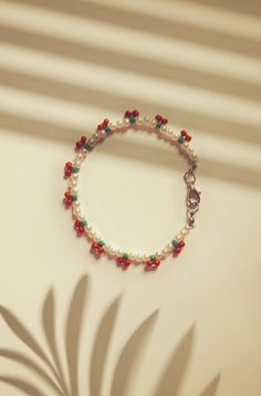 a white bracelet with red, green and blue beads sits next to a palm leaf