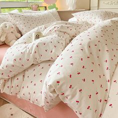 an unmade bed with white sheets and red flowers on it, in front of a window