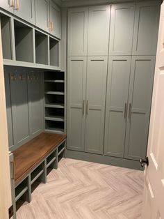 a large walk in closet with gray cabinets and wood bench next to it's doors