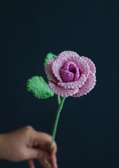 a crocheted pink flower being held by someone's hand on a dark background