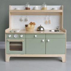 a wooden toy kitchen with an oven, sink and stove top on the floor in front of a gray wall