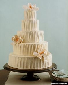 a three tiered white wedding cake with flowers on the top and bottom, sitting on a table