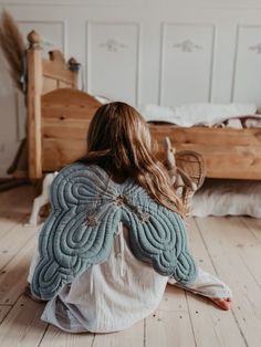 a woman sitting on the floor with her back turned to the camera and looking at an unmade bed