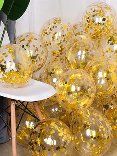 gold confetti filled balloons sitting on top of a chair next to a potted plant