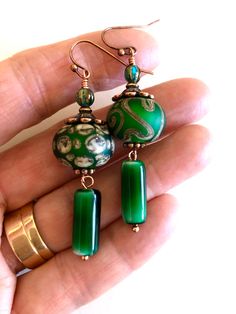 "Stunning artisan large lampwork rondelle bead earrings in Christmas green, taupe, and coppery gold accented with antique copper bead caps and ear wires. These beautiful handmade 15mm rondelles have a smooth matte finish with a slight iridescence. Slivers of glass and fine silver are used to \"draw\" the intricate designs. Beads are then fired at +900 degrees. The result is a gorgeous one of a kind lampwork bead. Beads are matched in size and color but have slightly different patterns on purpose Green Beaded Earrings With Large Beads For Gift, Green Artisan Round Bead Earrings, Artisan Green Beaded Earrings For Gift, Artisan Green Beaded Earrings As Gift, Handmade Green Copper Earrings, Handmade Copper Green Earrings, Unique Green Round Beads Earrings, Unique Green Round Beaded Earrings, Artisan Green Beaded Earrings Nickel Free