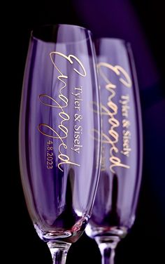 two wine glasses with writing on them sitting side by side in front of a black background