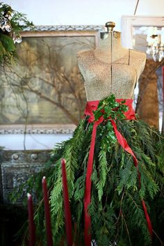 a mannequin is adorned with greenery and red ribbon