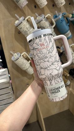 a person holding up a starbucks cup in front of a wall of coffee mugs