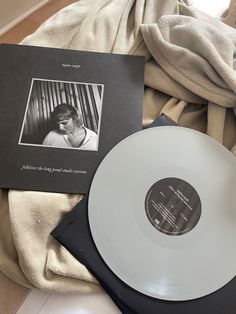 an album and record sitting on top of a bed next to a blanket with a woman's face